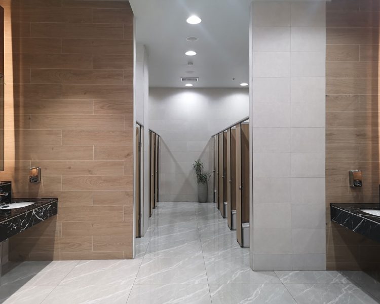 The interior of a sleek, modern public restroom featuring recessed ceiling lights, marble countertops, and tiled walls.