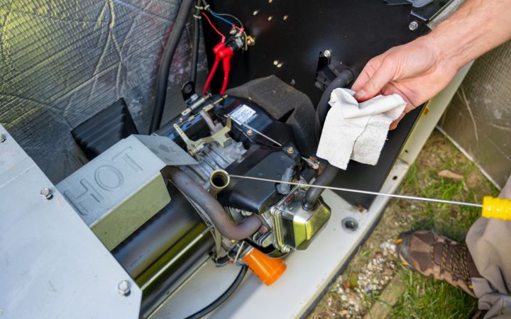 Technician performing routine maintenance on a generator engine, checking oil levels with a dipstick while holding a cleaning cloth, with exposed engine components and wiring visible